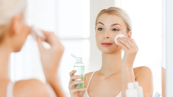 beauty, skin care and people concept - smiling young woman applying lotion to cotton disc for washing her face at bathroom; Shutterstock ID 388715125; PO: today.com